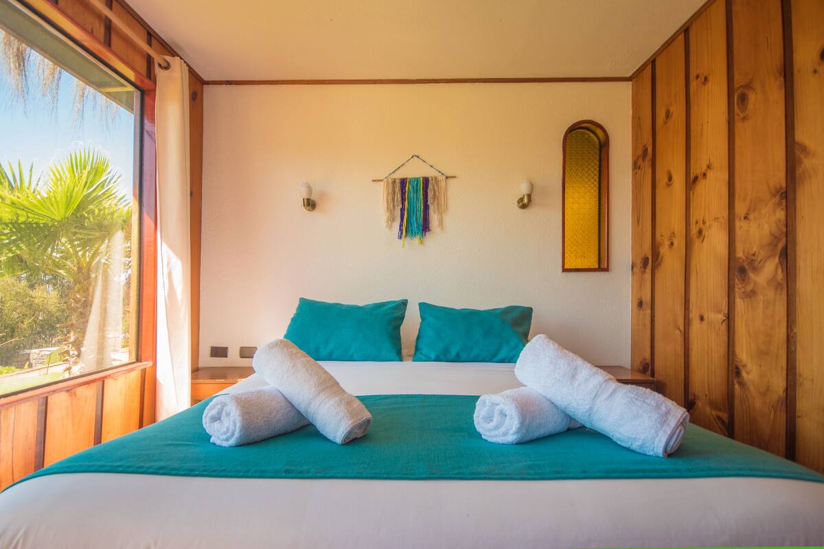 Una habitación de hotel con una cama, dos almohadas, un ventanal y una pared de madera.
