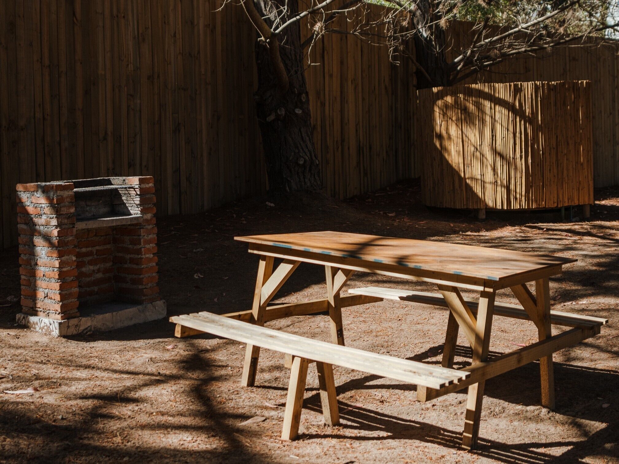 Una mesa de picnic de madera con bancos y una parrilla de ladrillo en un patio trasero.
