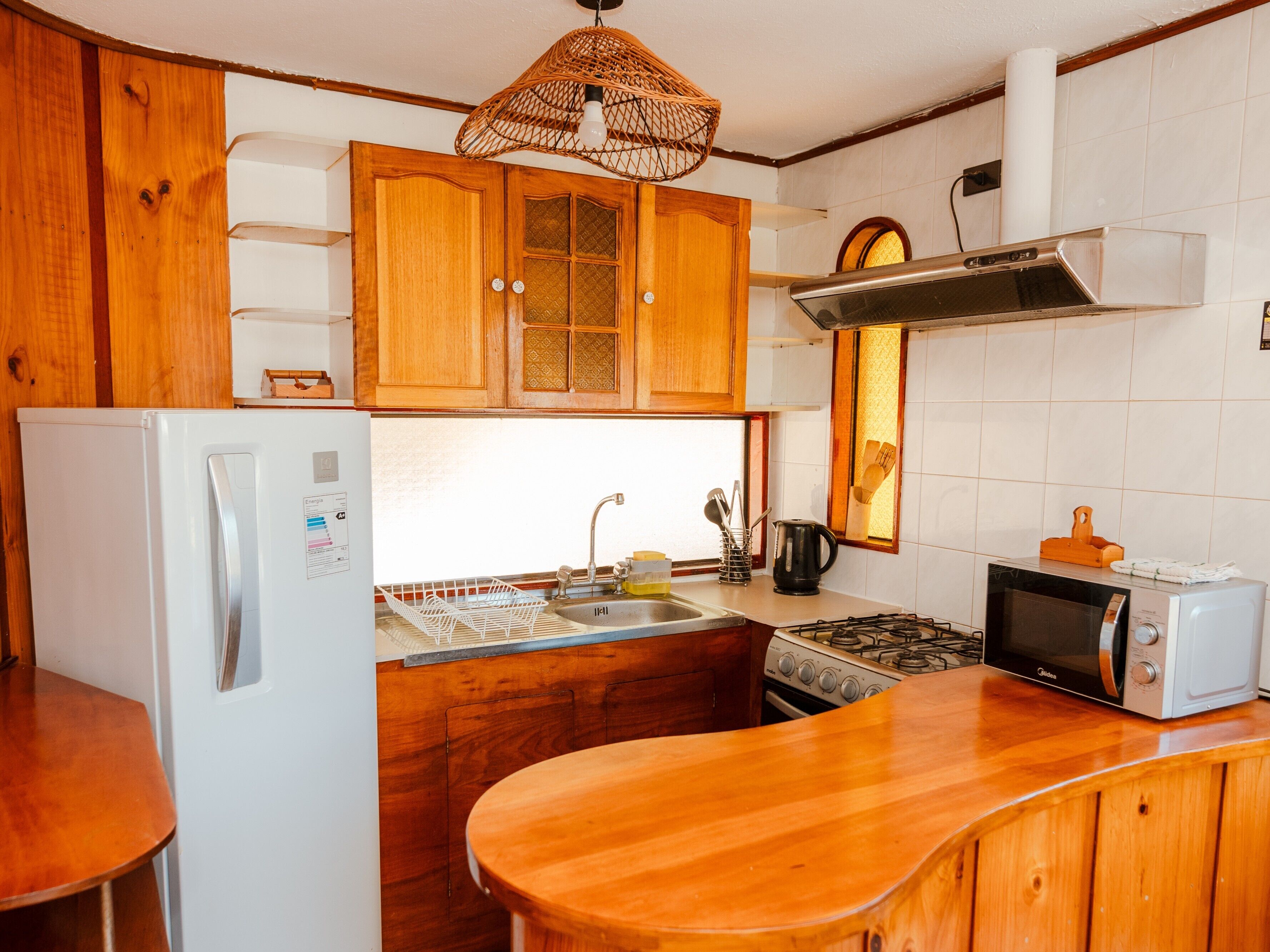 Een keuken met houten kastjes, een witte koelkast, een fornuis, een spoelbak en een magnetron.