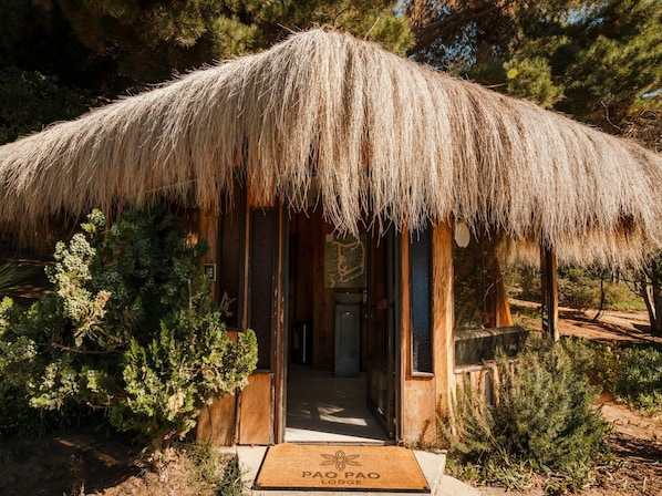 Una estructura de techo de paja con entrada de madera, rodeada de follaje.