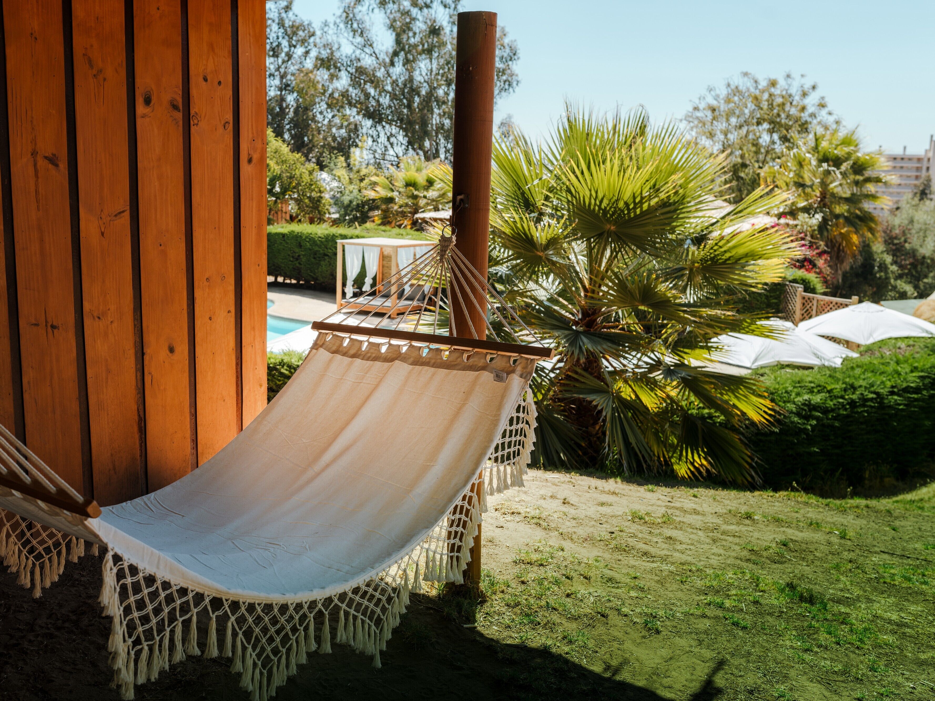 A hammock chair attached to a wooden structure, with a pool and greenery in the background.