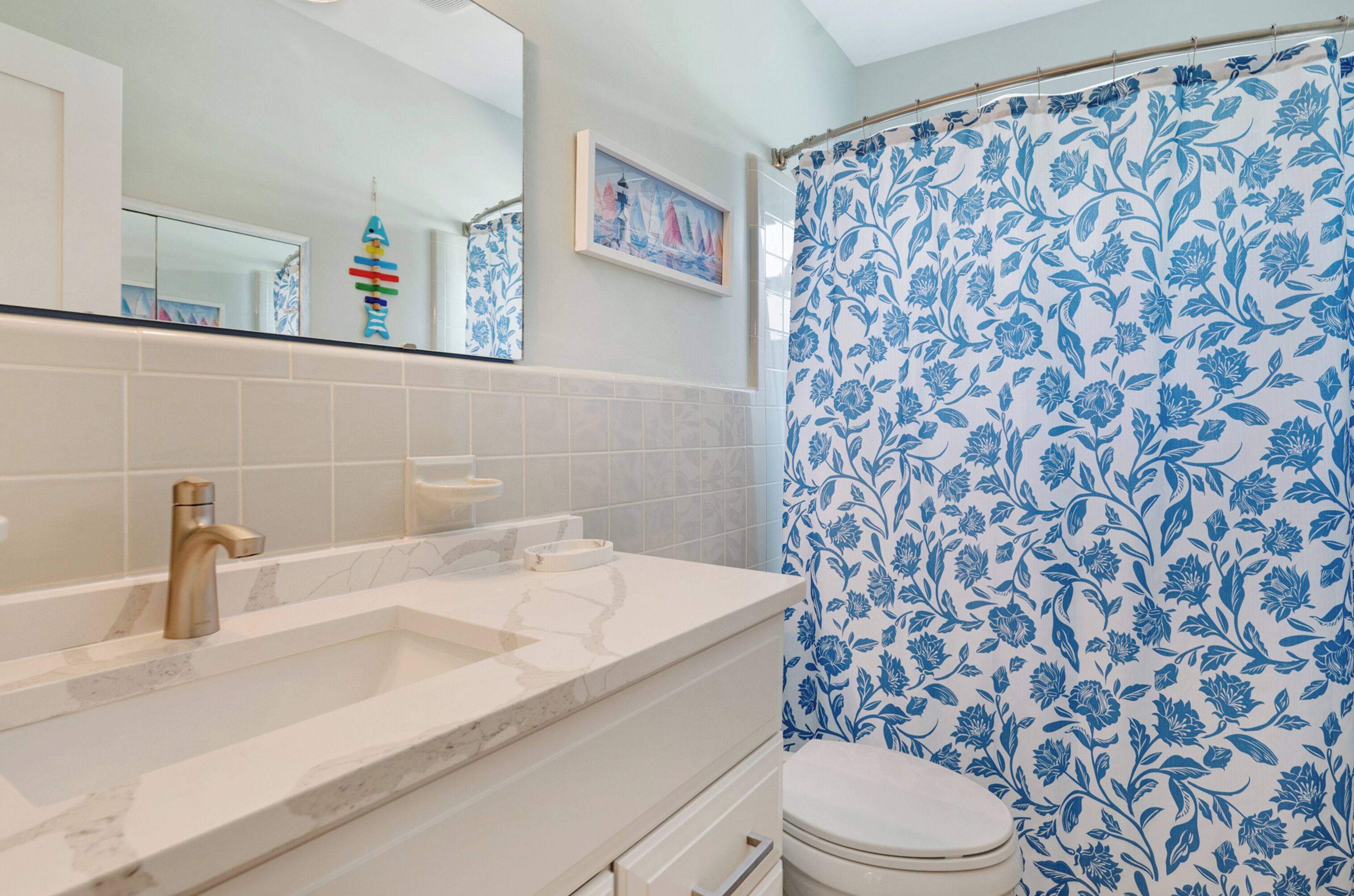 Un baño con lavamanos, espejo, inodoro y cortina de ducha con estampado floral.