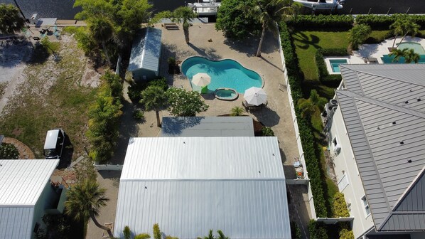 An aerial view of a residential area with a swimming pool, a covered patio, and a small boat dock.