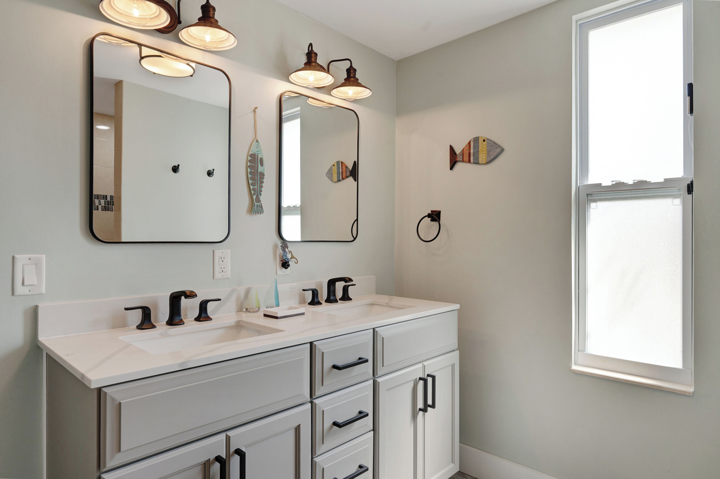 A bathroom with a white vanity, two mirrors, and a window.