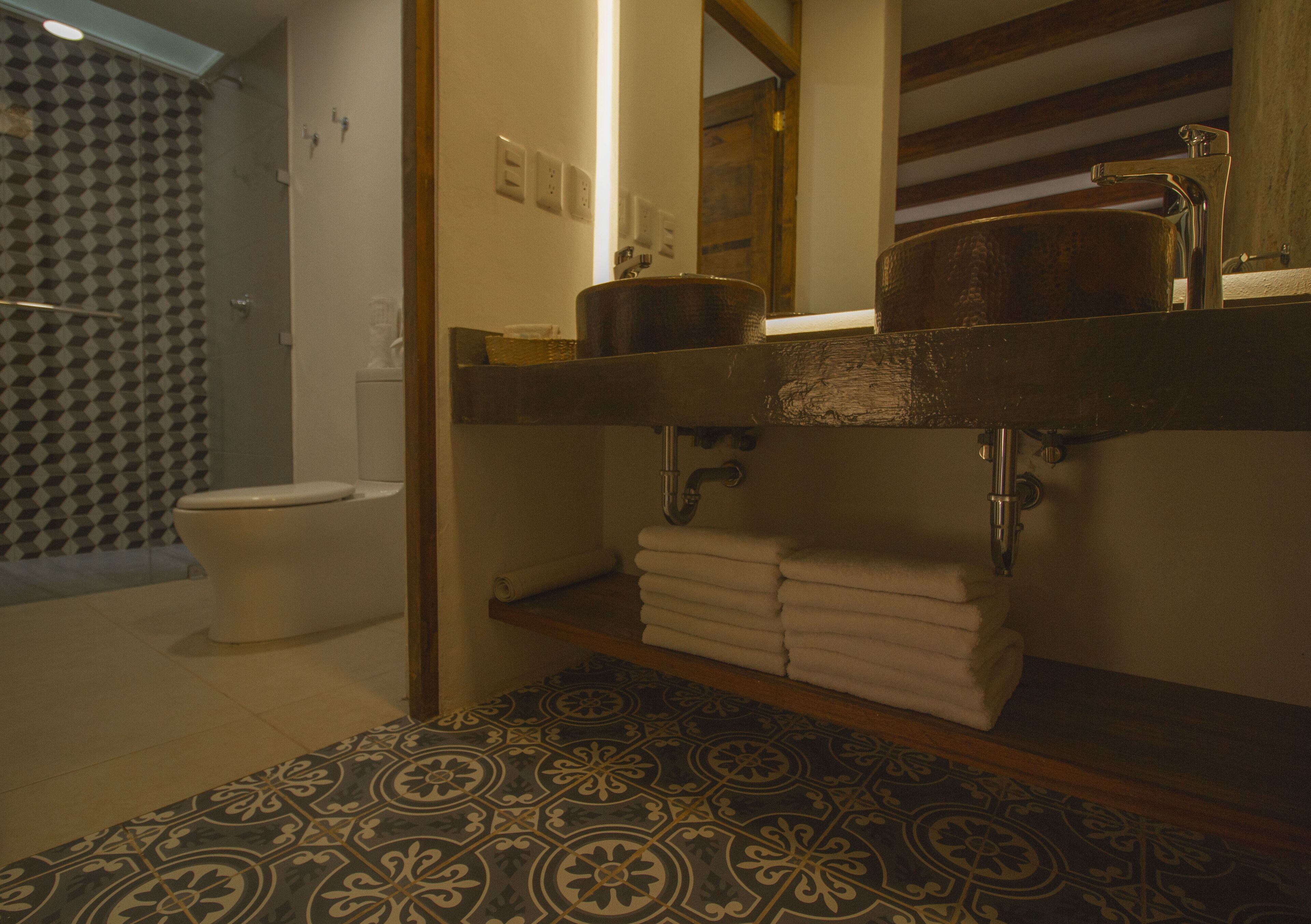 A bathroom with a patterned floor, a toilet, a sink with a mirror, and a shower area.