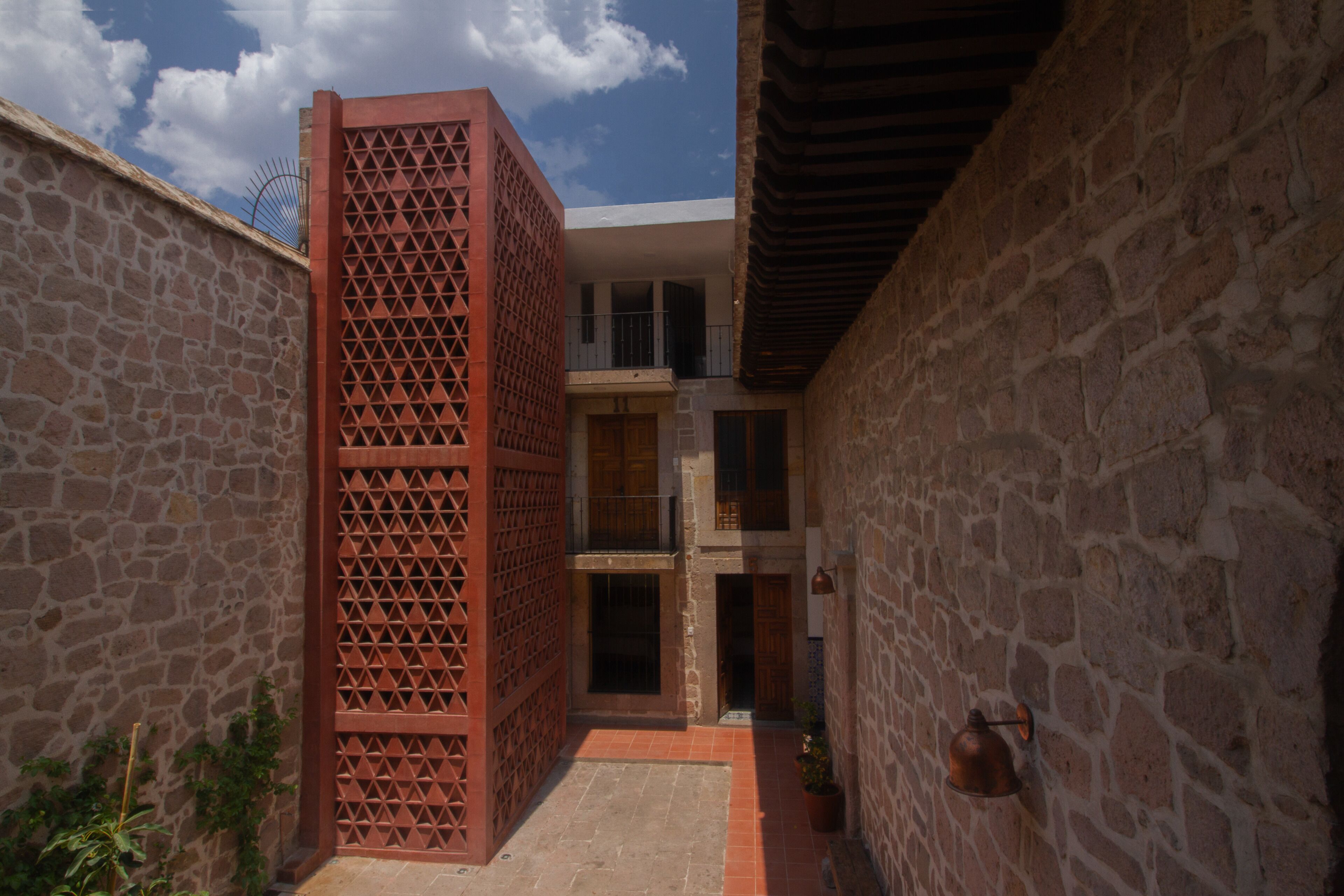 Un patio estrecho con muros de piedra, una estructura de celosía roja y un pequeño jardín.