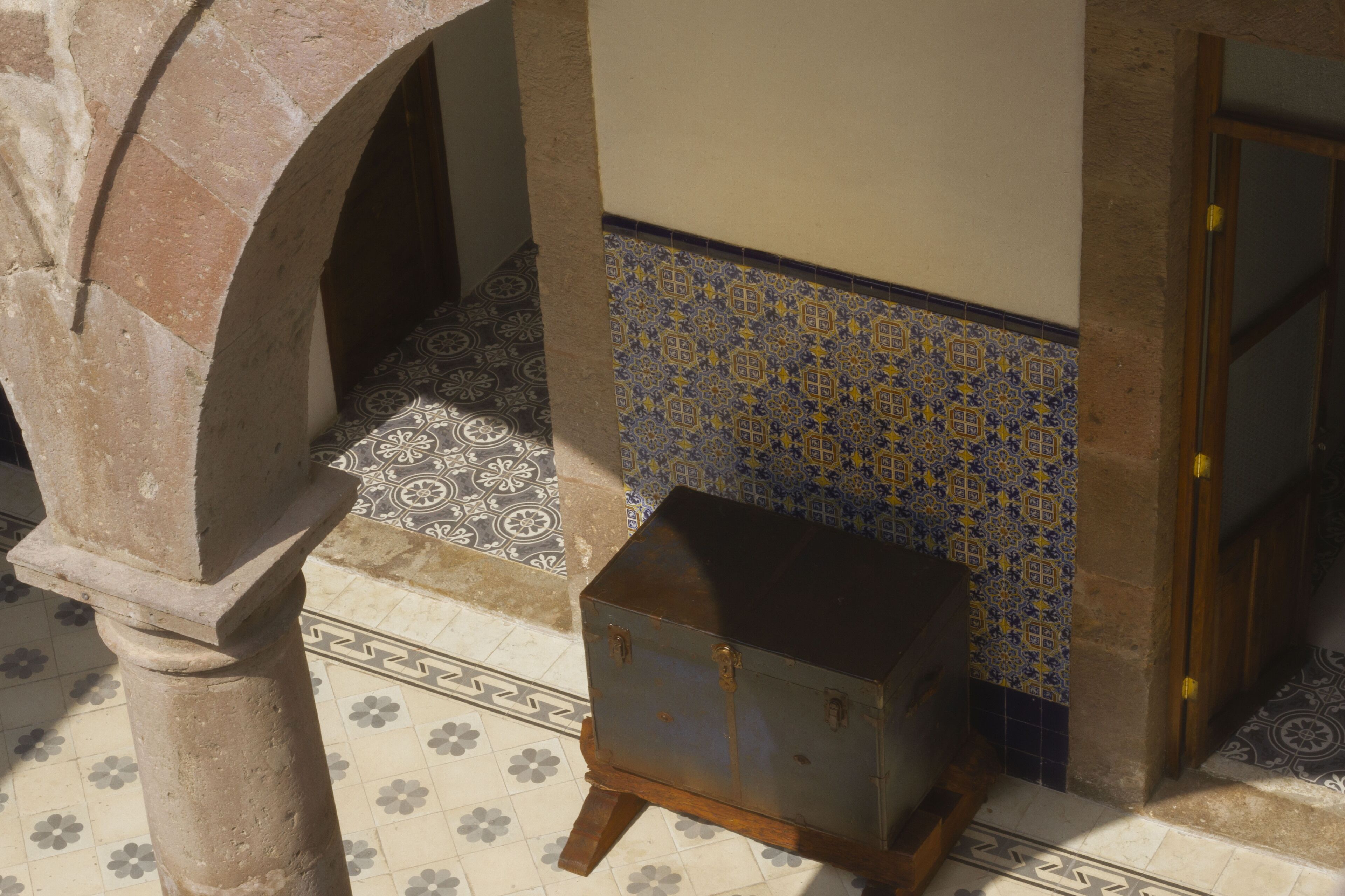 A tiled floor with a geometric pattern, a stone column, and a small wooden chest.