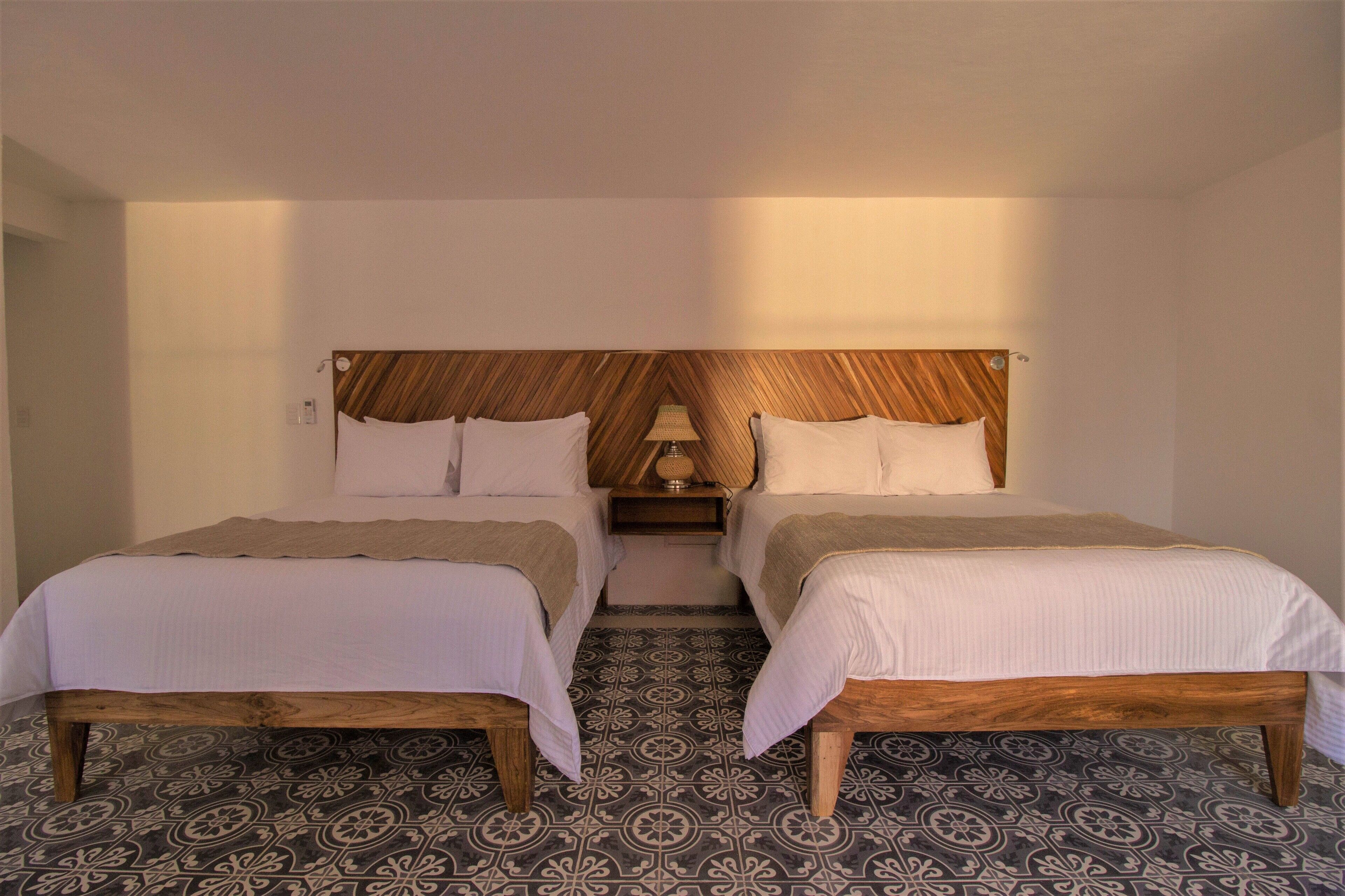 Habitación doble con dos camas, cabecero de madera, pisos de baldosas estampadas y una mesita de noche con lámpara.