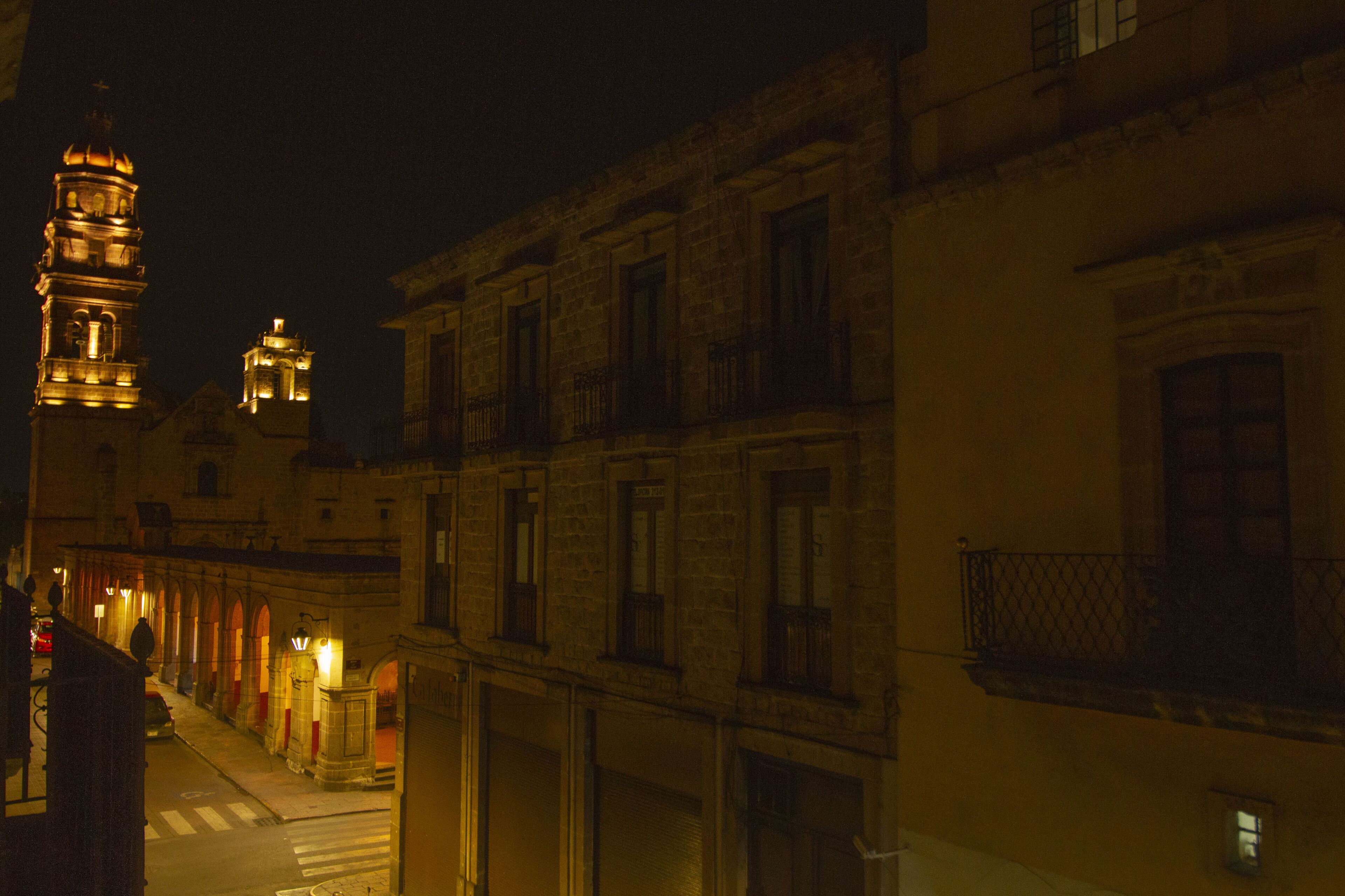 A nighttime street view with illuminated buildings and a prominent tower.