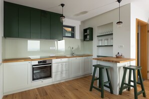 A modern kitchen with white cabinets, a wooden countertop, and two green stools.