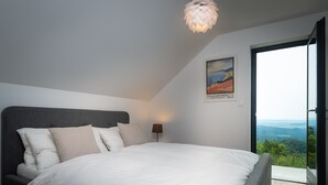 Une chambre à coucher avec un grand lit, une tête de lit, une lampe de chevet, un tableau encadré et une vue à travers une porte vitrée.