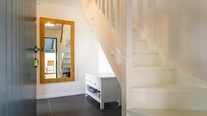 Un escalier menant à un palier avec un mur blanc et un miroir qui reflète une pièce.