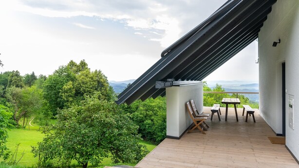 Un balcon avec une table et des chaises, donnant sur un paysage verdoyant et luxuriant et sur des montagnes lointaines.