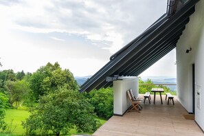 Ein Balkon mit Tisch und Stühlen, mit Blick auf eine üppige grüne Landschaft und ferne Berge.