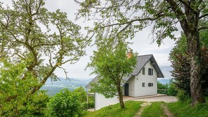Une maison blanche avec un toit en pente, entourée d’une végétation luxuriante et offrant une vue dégagée sur les montagnes lointaines.