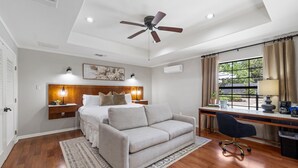 Ein Schlafzimmer mit einem Bett, einem Schreibtisch, einem Stuhl, einem Deckenventilator und einem Fenster mit Vorhängen.