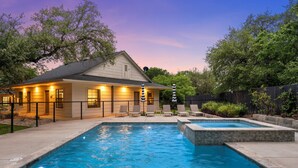 Ein Wohnhausgarten mit Swimmingpool, einer überdachten Terrasse und einem eingezäunten Bereich mit Liegestühlen.
