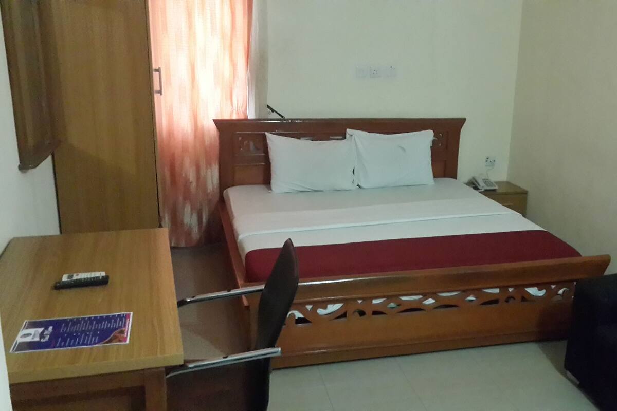 A hotel room with a bed, a desk with a chair, a telephone, and a curtain.