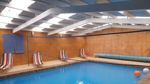 An indoor swimming pool with clear blue water, a ceiling with skylights, and striped beach chairs along the poolside. - Idyllic Tuscan Paradise with Magical Gardens (Tantanoola)