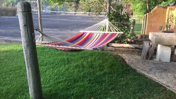 Relax in a hammock suspended between two posts, overlooking a serene lawn and a tree with vibrant flowers.
