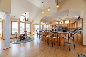 A spacious kitchen with high ceilings, a central island with bar stools, and wooden cabinetry. - Summer Winds - Corolla, Whalehead, 300 Yds to Beach, Elevator, Pool, Hot Tub, Pets OK (Corolla)