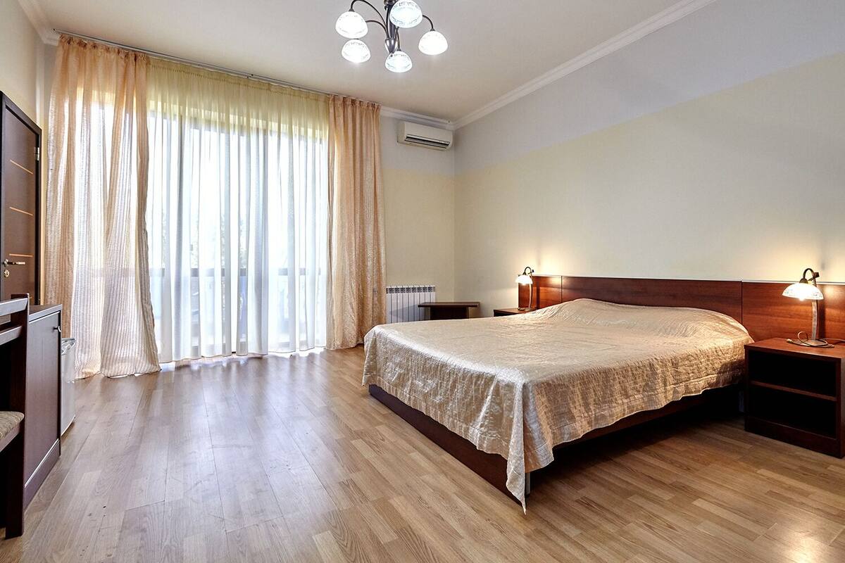 Un dormitorio con una cama grande, cabecera de madera, mesitas de noche con lámparas, un armario y una ventana con cortinas.