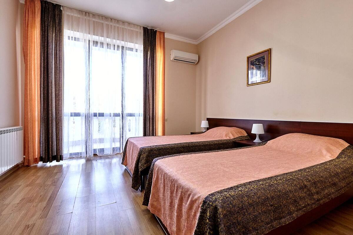 Habitación de hotel con dos camas, una ventana con cortinas, un equipo de aire acondicionado y un cuadro en la pared.