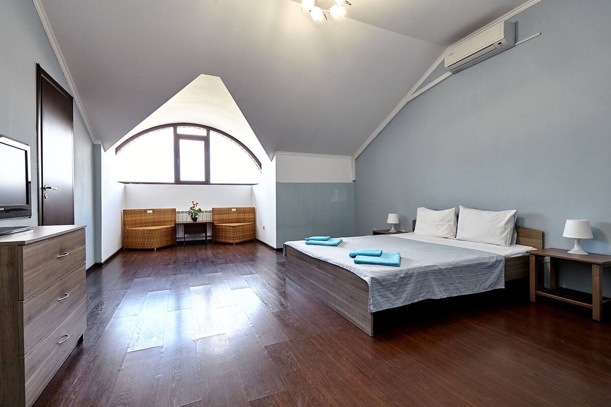 Un dormitorio con una cama grande, un escritorio, sillas de mimbre y un televisor.