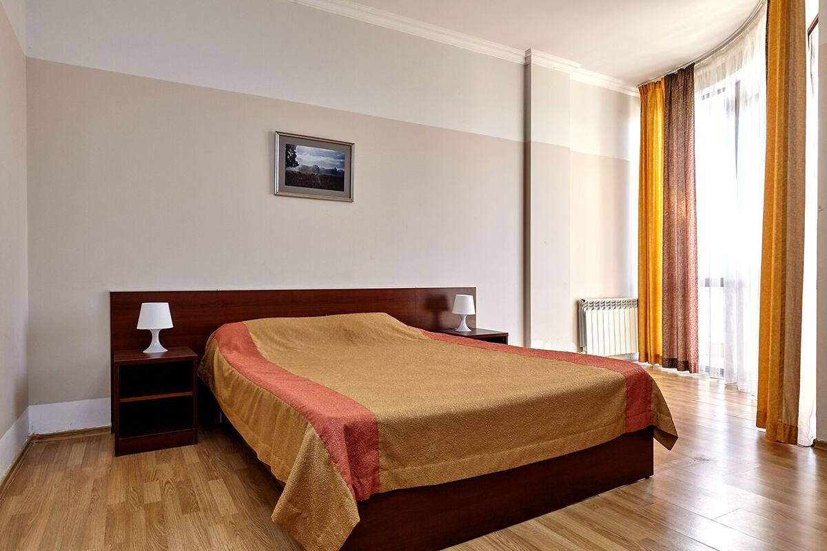 Una cama bien hecha en una habitación de hotel, con cabecera de madera, una mesita de noche con una lámpara y un cuadro enmarcado en la pared.