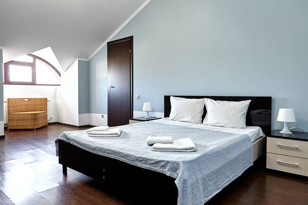 Un dormitorio con cama, mesitas de noche, una silla de mimbre y una puerta.