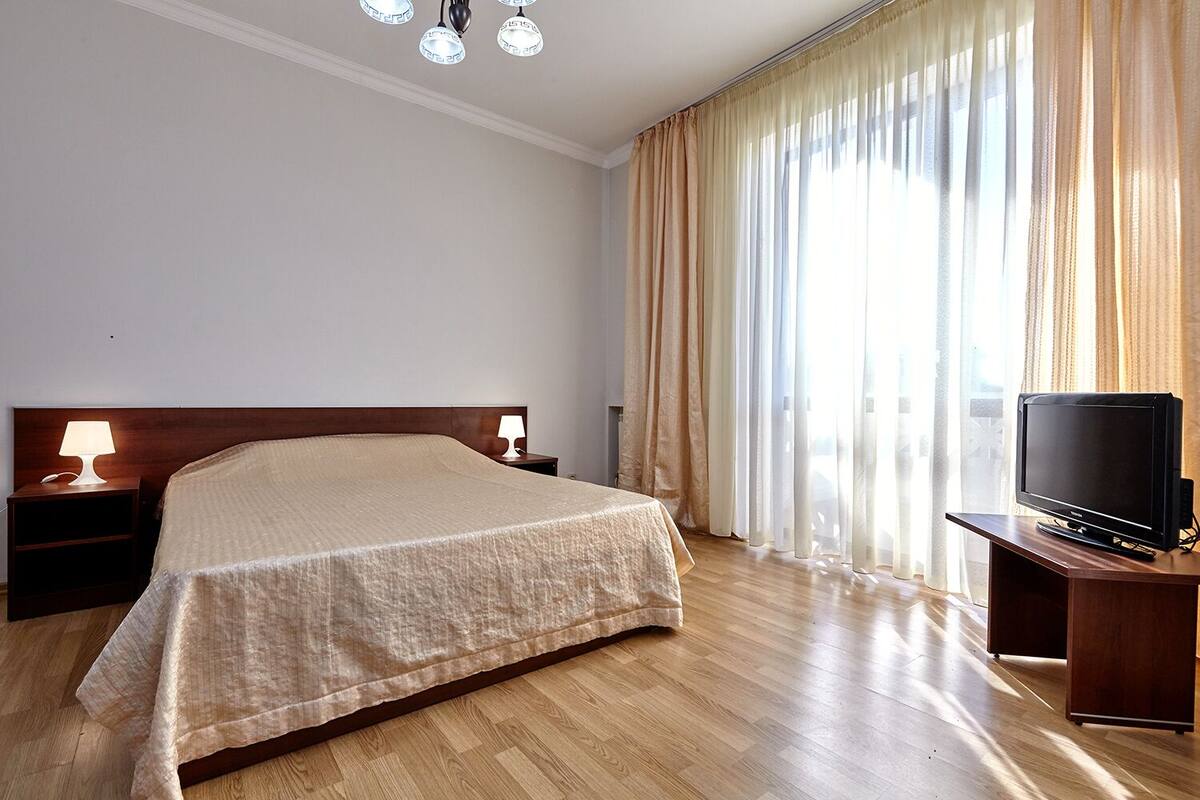 Habitación de hotel con una cama grande, un televisor sobre un soporte de madera y una mesita de noche con lámpara.