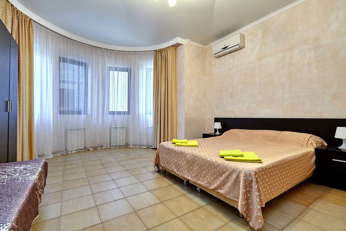 Una habitación de hotel con cama, mesita de noche, lámpara, ventana con cortinas y aire acondicionado.
