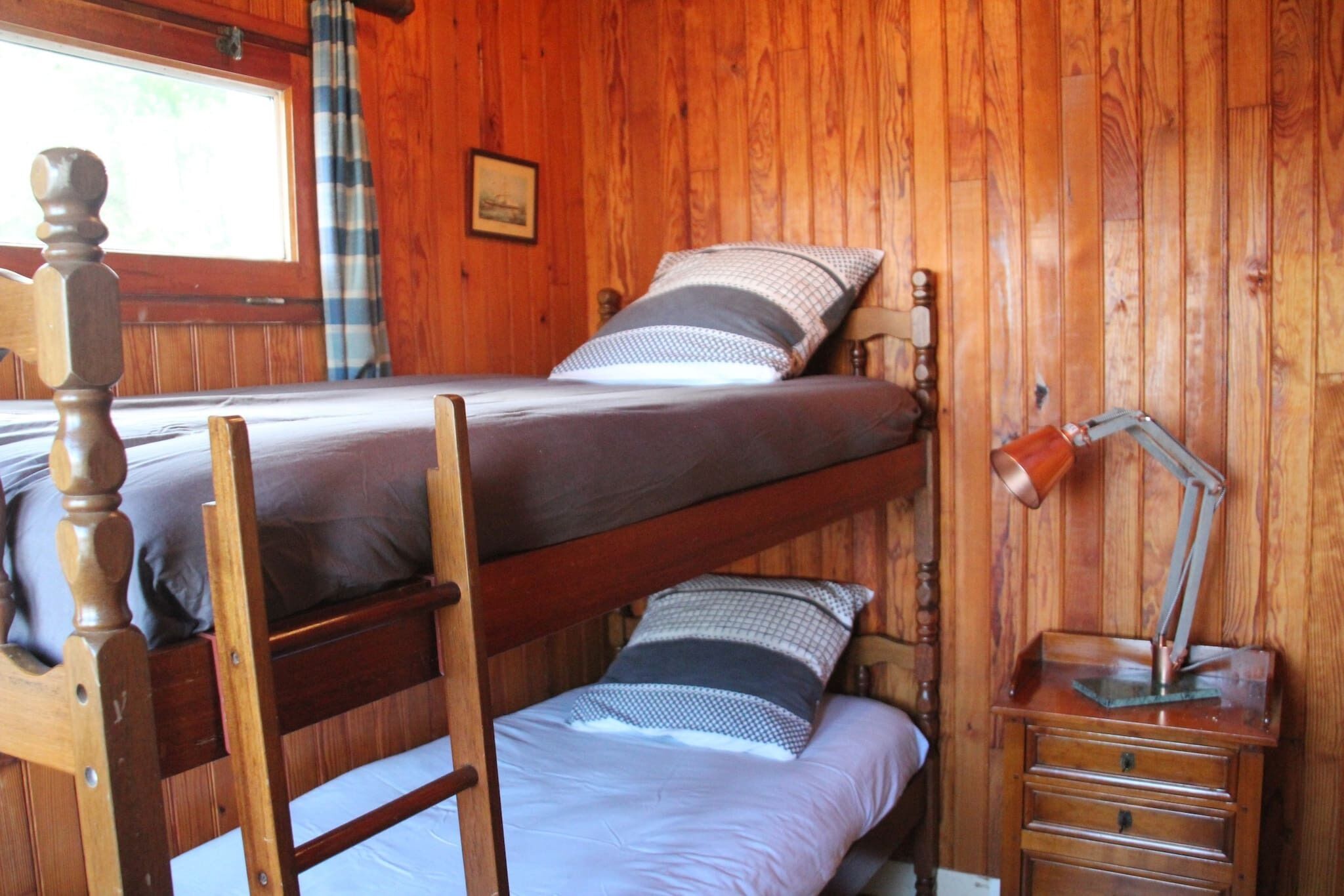 Una cama nido con cabecera de madera, un escritorio con lámpara y una ventana con cortinas.