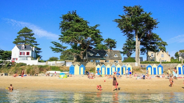 Une plage avec des gens, un ciel dégagé et des bâtiments en arrière-plan.