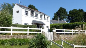 Une maison blanche à deux étages, avec un mur en pierre et une clôture blanche à l’avant.