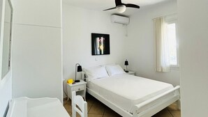 A bedroom with a bed, a desk, a chair, a ceiling fan, and a window. - Drafies House (Mykonos)