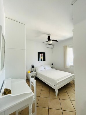 A bedroom with a bed, a desk, a chair, a ceiling fan, and a window.