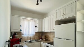 A compact kitchen with white cabinets, a red kettle, a stove, and a refrigerator. - Drafies House (Mykonos)