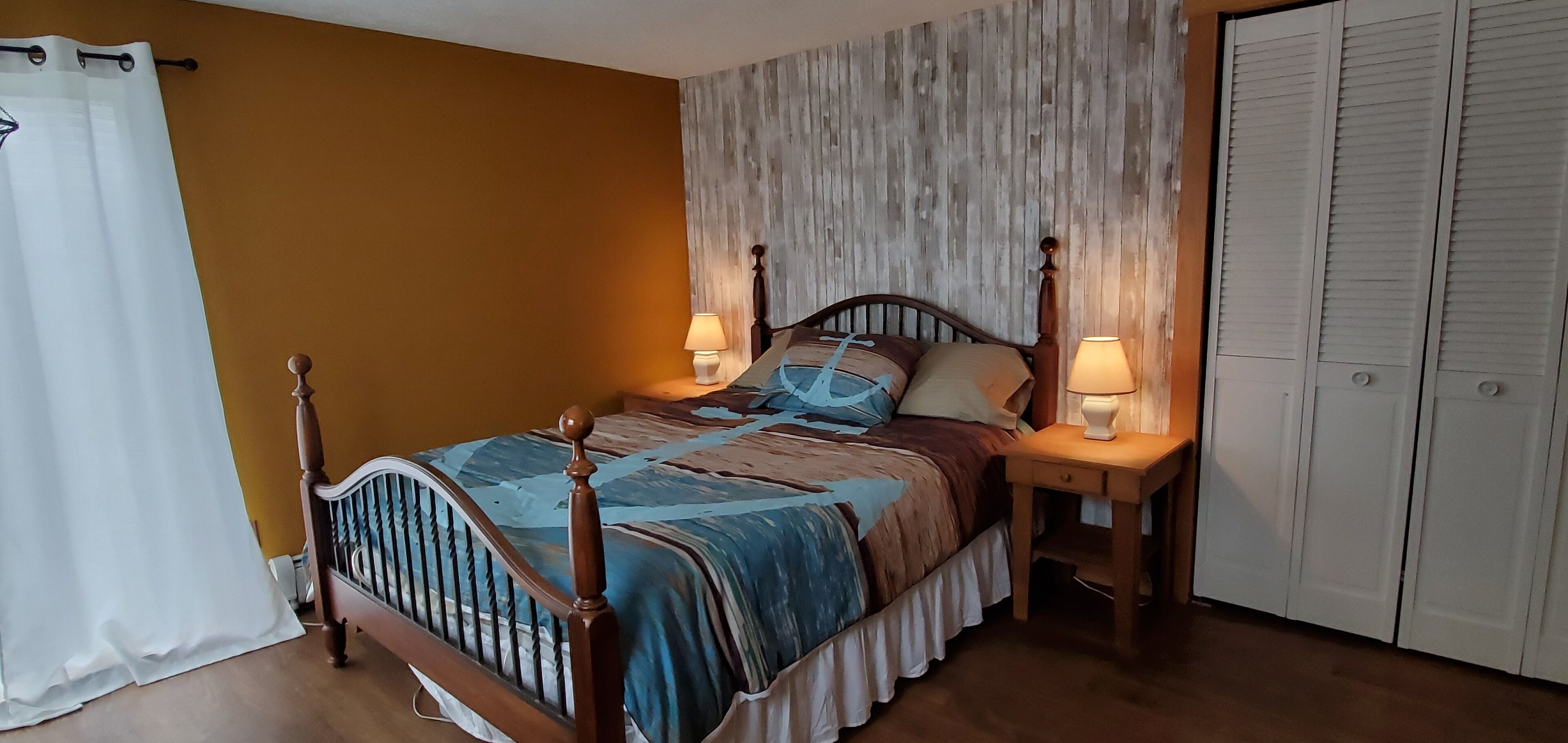 A bedroom with a wooden bed, two bedside lamps, a white wardrobe, and a curtain.