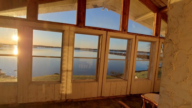 A room with large windows overlooking a calm body of water, wooden beams, and a rustic interior. - Year-Round: Amazing Sunrises, 150ft Shore, Private Boat Launch/Dock, Hot Fishing (Alburg)