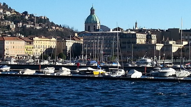 A marina with boats docked, a prominent building with a dome in the background, and a hilly landscape.