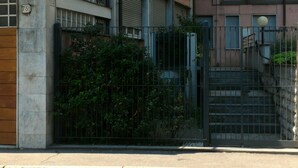 A gated entrance with a metal fence, a staircase leading to a building with a pink facade, and a number '75' sign on a column.