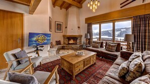A cozy living room with a fireplace, wooden furniture, and a large window offering a view of the mountains. - Chalet Coeur - Jacuzzi - Sauna - Views - La Tzoumaz, 4 Vallees (La Tzoumaz)