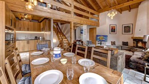 A spacious dining area with a wooden table set for four, a staircase leading to an upper level, and a cozy living area with a fireplace. - Chalet Coeur - Jacuzzi - Sauna - Views - La Tzoumaz, 4 Vallees (La Tzoumaz)