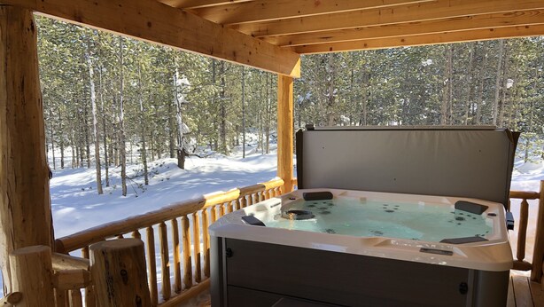Une terrasse en bois avec un jacuzzi, des marches et une vue sur une forêt enneigée.