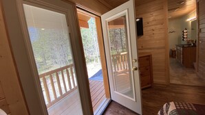 Un intérieur en bois avec une porte-fenêtre coulissante donnant sur une terrasse extérieure, une petite kitchenette et un coin salon confortable agrémenté d’un tapis à motifs.