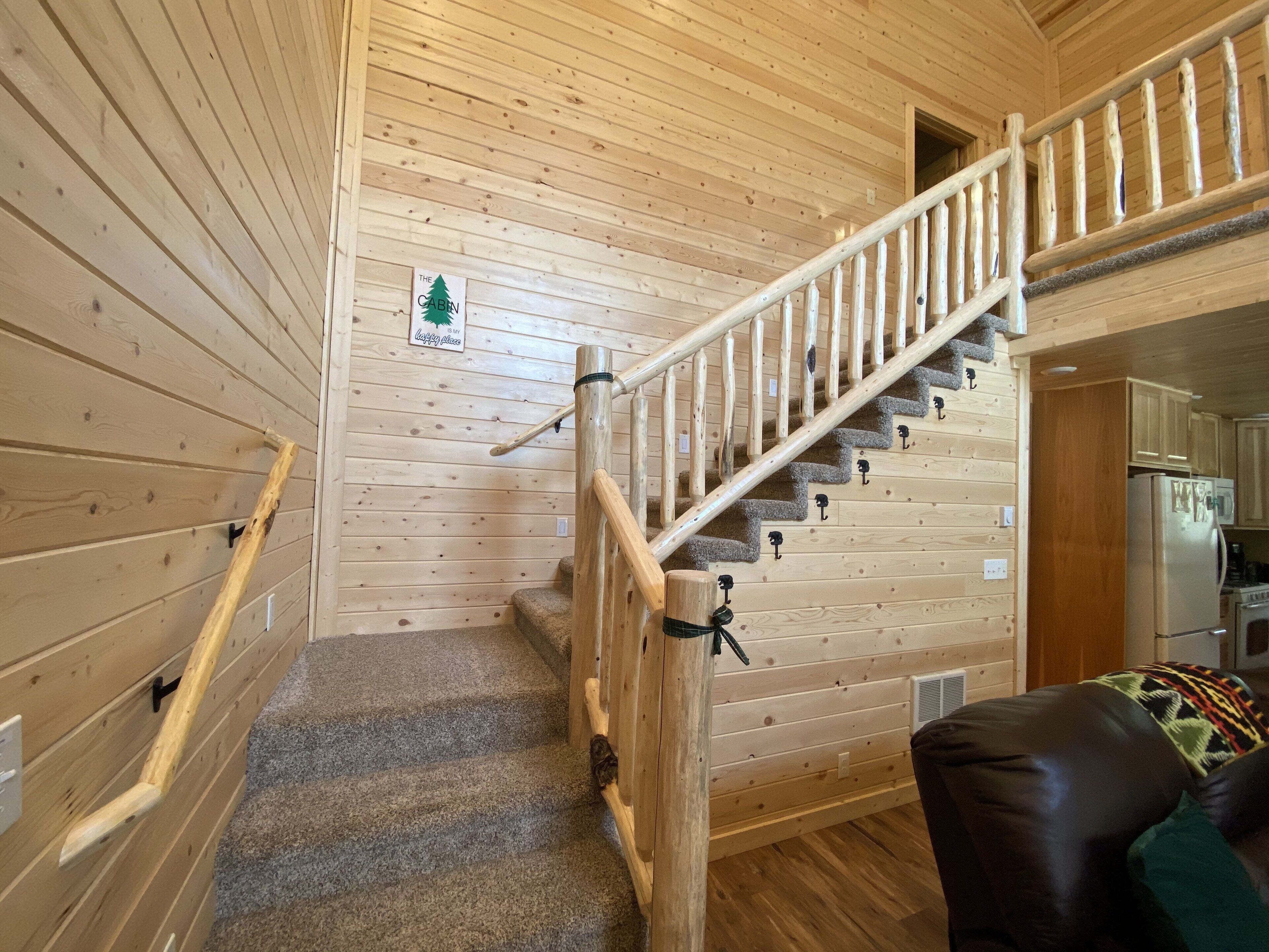 A wooden interior with a staircase, a sign reading "The Cabin is my happy place," and a kitchen area.