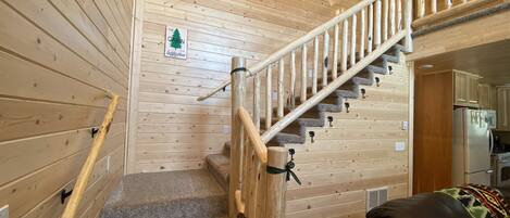 A wooden interior with a staircase, a sign reading "The Cabin is my happy place," and a kitchen area.