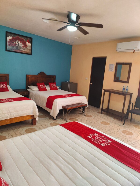 Habitación de hotel con dos camas, ventilador de techo, un cuadro, escritorio con dos botellas de agua y aire acondicionado.