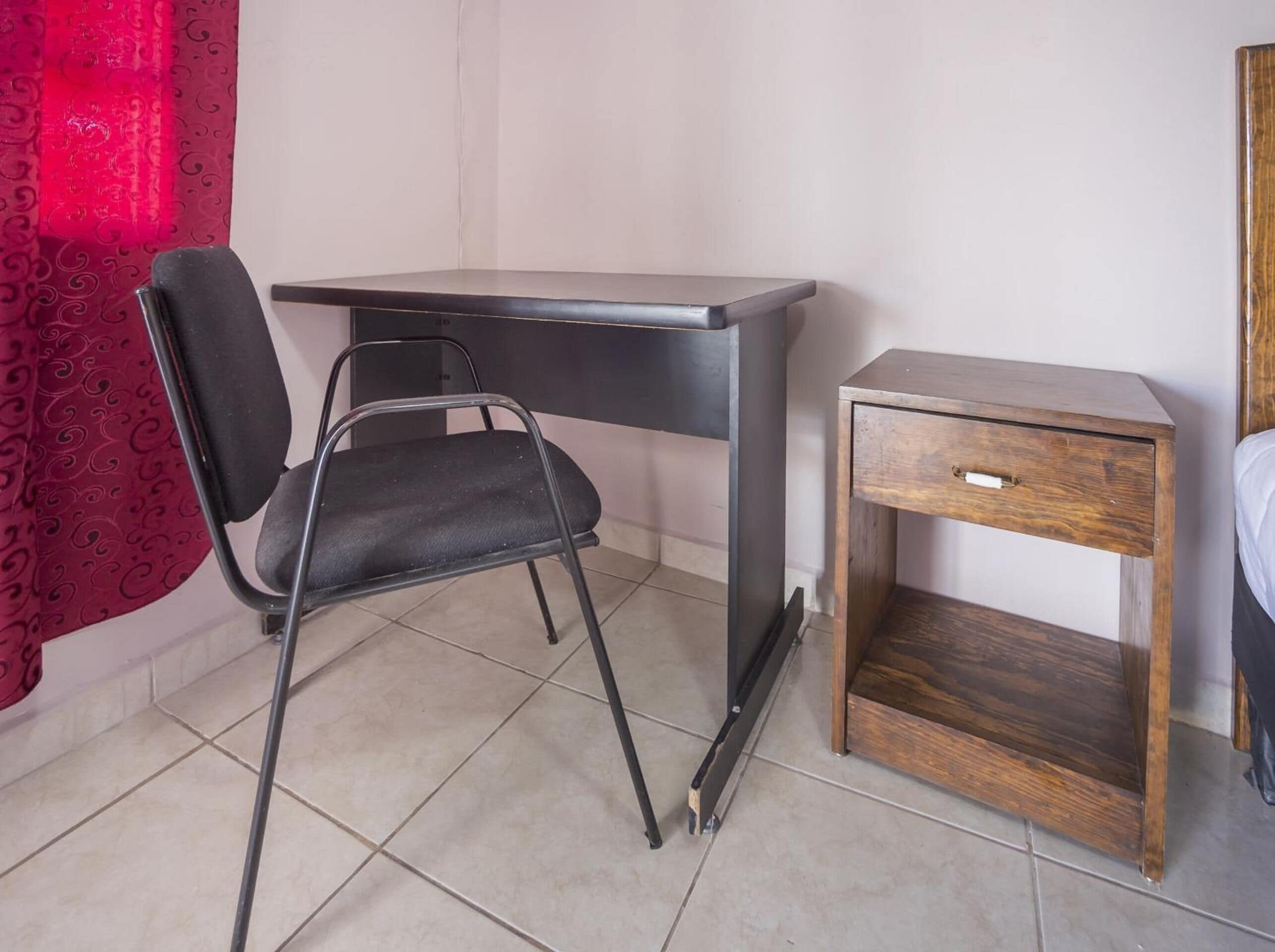 A small room with a desk, a chair, and a bedside table.